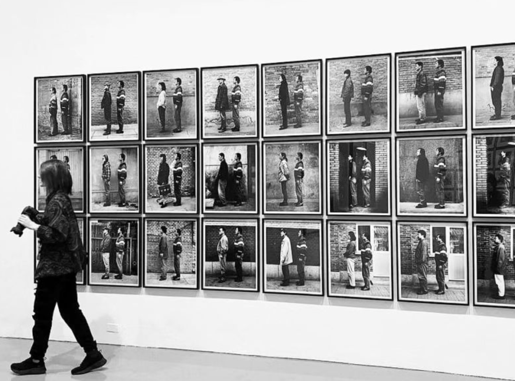 Pictured: Me, walking in front of a photography exhibit, at the Hirshorn Gallery in Dc. I am at far left with my camera. Black and White. 